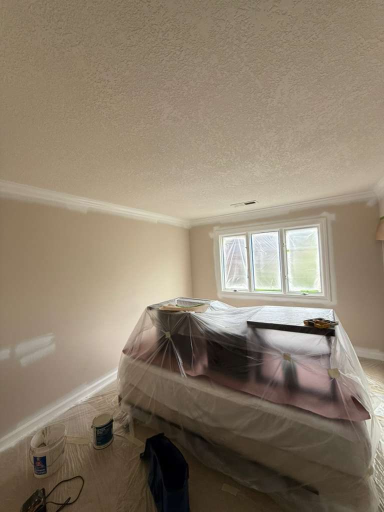 Room mid-project with all furniture plastic-wrapped and floors fully tarped, walls and trim being repainted